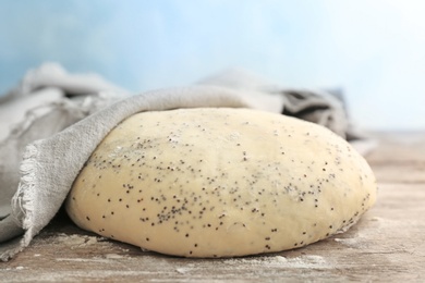 Raw dough with poppy seeds under towel on wooden table