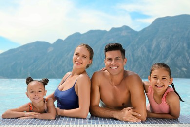 Happy family in outdoor swimming pool at luxury resort with beautiful view of mountains on sunny day