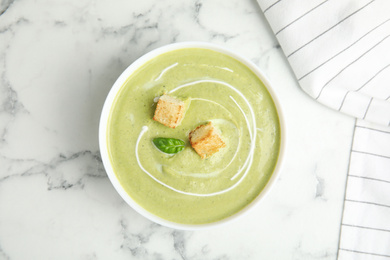 Delicious broccoli cream soup with croutons served on white marble table, top view