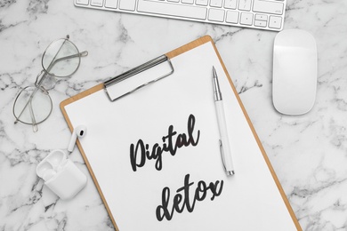 Flat lay composition of clipboard with phrase DIGITAL DETOX on white marble table
