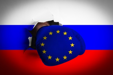 Man in boxing glove with European union stars punching hole through Russian flag, closeup. Political feud
