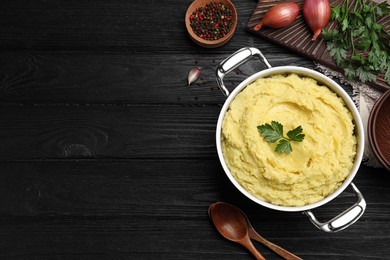 Photo of Pot of tasty mashed potatoes with parsley on black wooden table, flat lay. Space for text