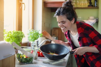 Young woman holding pan with freshly fried eggs and vegetables in kitchen