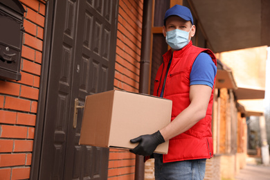Courier in protective mask and gloves with box near house entrance. Delivery service during coronavirus quarantine