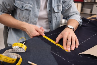 Tailor working with fabric at table in workshop, closeup