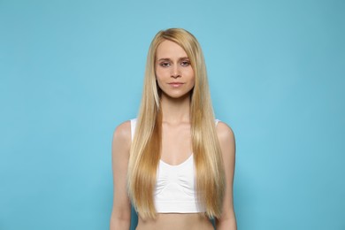 Beautiful young woman with long straight hair on light blue background