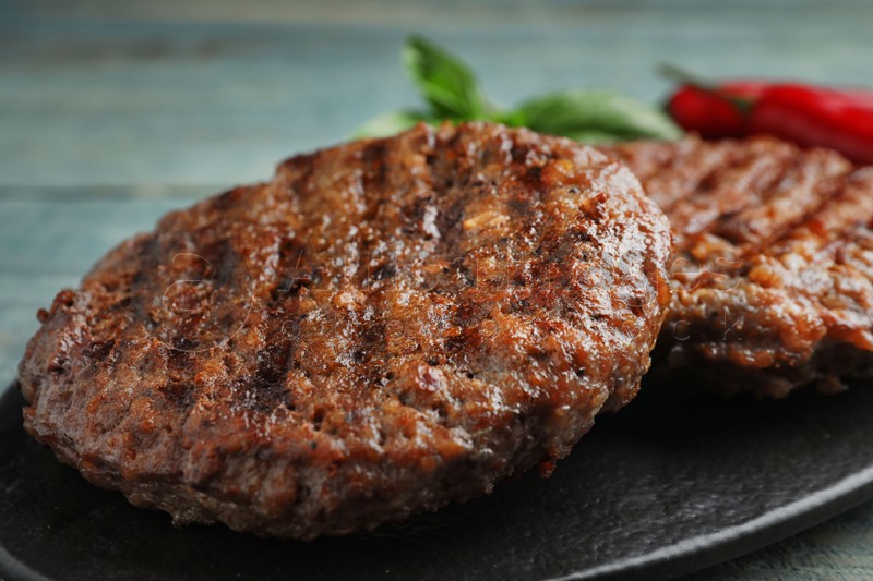 Grilled meat cutlets for burger on blue wooden table, closeup