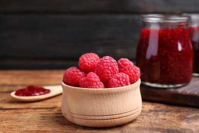 Photo of Fresh raspberries in bowl and jam on wooden table, closeup