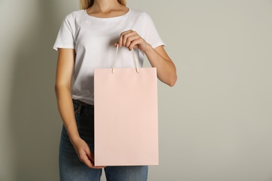 Woman with paper shopping bag on light grey background, closeup