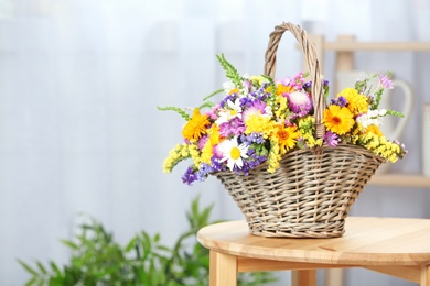 Wicker basket with beautiful wild flowers on table indoors