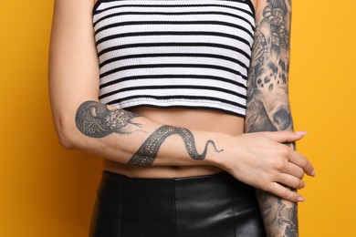 Photo of Woman with tattoos on arms against yellow background, closeup