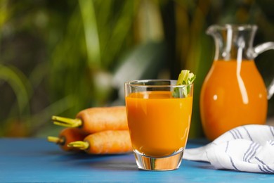 Photo of Tasty carrot juice on blue wooden table outdoors
