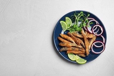 Photo of Plate with delicious fried anchovies, lime slices, microgreens and onion rings on light table, top view. Space for text