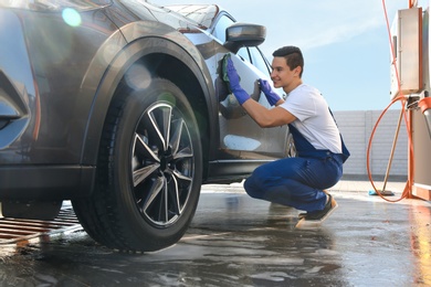 Male worker cleaning automobile door with rag at car wash