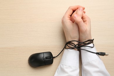 Man showing hands tied with computer mouse cable at wooden table, top view. Internet addiction