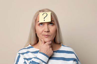 Emotional mature woman with question mark on beige background