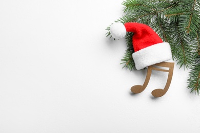 Decorative music note with Santa hat near fir tree branch and space for text on white wooden background, top view. Christmas celebration
