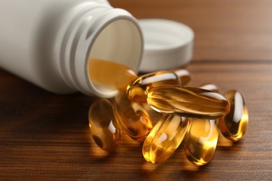 Overturned bottle with dietary supplement capsules on wooden table, closeup