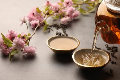 Photo of Traditional ceremony. Pouring brewed tea from teapot into cup on grey table, closeup