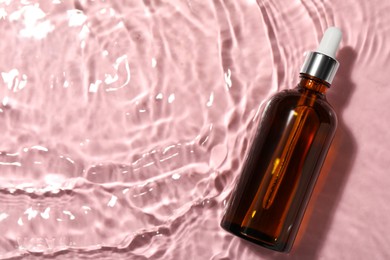 Bottle of hydrophilic oil in water on pink background, top view. Space for text