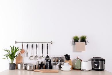 Set of clean cookware, dishes, utensils and appliances on table at white wall