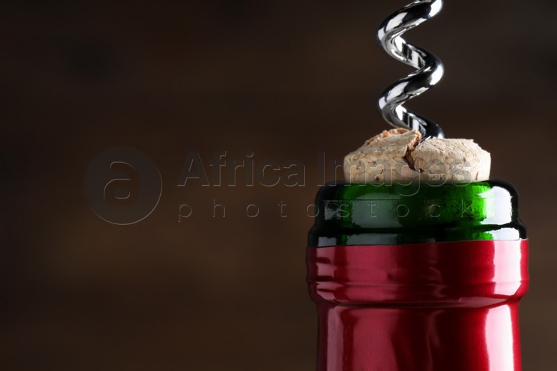 Photo of Opening wine bottle with corkscrew on dark brown background, closeup. Space for text