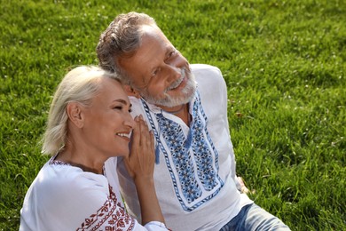 Photo of Happy mature couple in Ukrainian national clothes resting on green grass outdoors