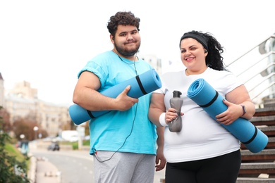 Overweight couple in sportswear with mats outdoors