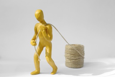Human figure made of yellow plasticine carrying rope on white background