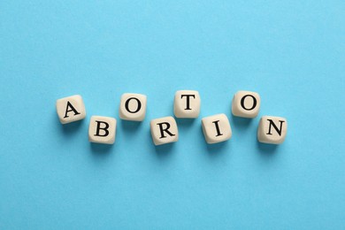 Word Abortion made of wooden cubes on light blue background, flat lay