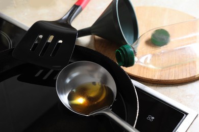 Frying pan of used cooking oil with ladle, empty bottle and funnel in kitchen, closeup