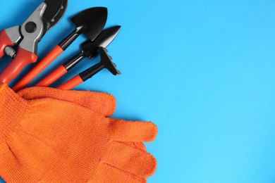 Gardening gloves and tools on light blue background, flat lay. Space for text