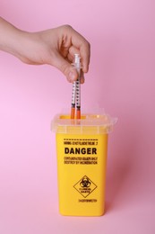 Woman throwing used syringes into sharps container  on pink background, closeup
