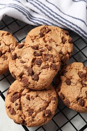 Photo of Cooling rack with delicious chocolate chip cookies on white table, closeup