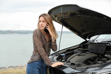 Photo of Troubled young woman talking on phone near broken car outdoors