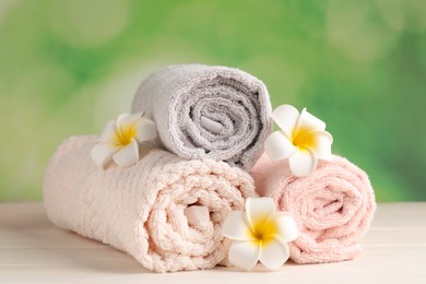 Soft folded towels and plumeria flowers on white wooden table