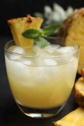 Photo of Delicious fresh pineapple juice with mint and ice cubes on black table, closeup