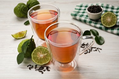 Glass cups of tasty bergamot tea and fruit on white wooden table