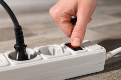 Man pressing power button of extension board on floor, closeup