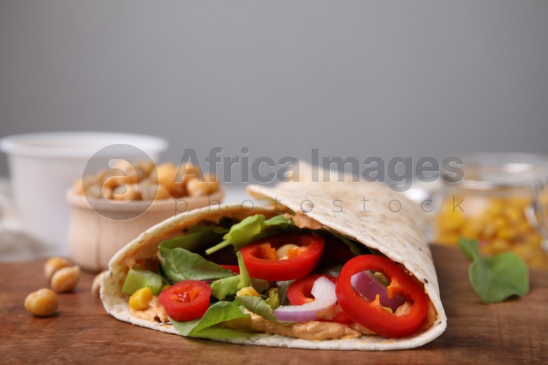 Photo of Delicious hummus wrap with vegetables on wooden board, closeup. Space for text