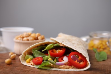 Delicious hummus wrap with vegetables on wooden board, closeup. Space for text