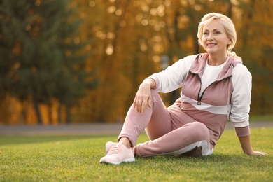 Happy mature woman sitting on grass in park
