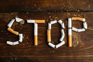 Word Stop of cut cigarettes on wooden table, flat lay. Quitting smoking concept