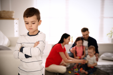 Unhappy little boy feeling jealous while parents spending time with other children at home