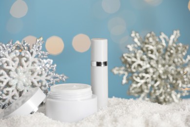 Jar of hand cream and lip balm near decorative snowflakes on snow against blurred lights. Winter skin care cosmetics