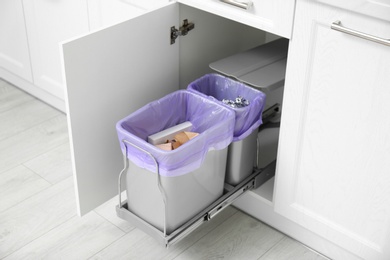 Open cabinet with full trash bins for separate waste collection in kitchen