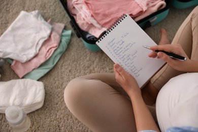 Pregnant woman writing packing list for maternity hospital at home, above view