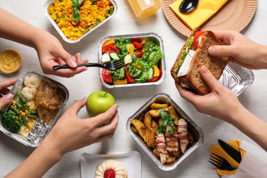 People with lunchboxes at white wooden table, top view. Healthy food delivery