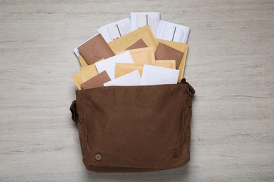 Brown postman bag with newspapers and mails on white wooden table, flat lay