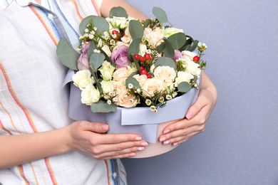 Female florist holding box with flowers on grey background